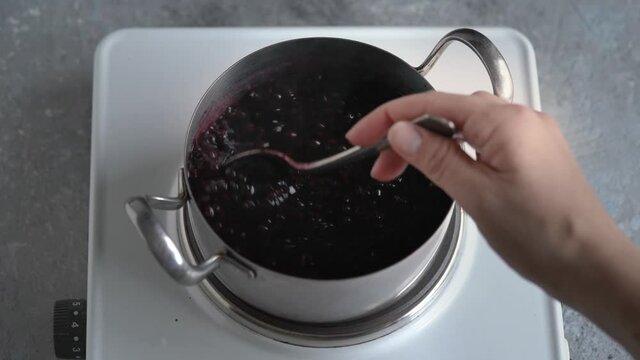 Crushed elderberries are being cooked with spices - Preparation of homemade black elder syrup