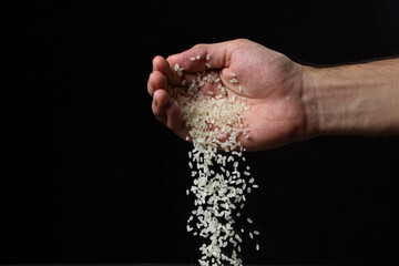 Rice groats on a black background. Rice is pouring out of hand on a dark background