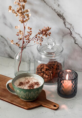 Morning cozy kitchen interior. Cappuccino, lit candle, cookies in a jar, dried flowers in a vase on...