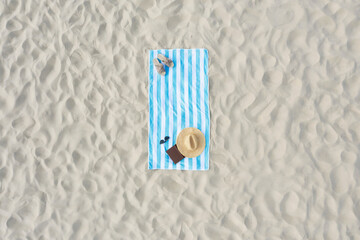 Striped beach towel with straw hat, book, sunglasses and slippers on sand, aerial view