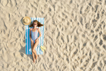 Woman sunbathing on beach towel at sandy coast, aerial view. Space for text