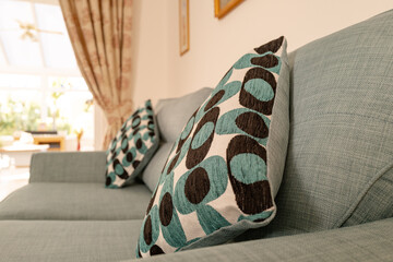 Shallow focus view of patterned cushions seen on a fabric sofa. Seen in a sunny living room, a conservatory is visible in the distance.