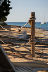 Wooden pole with ropes at the beach with view to sea and yacht. Calm atmosphere at the evening resort.