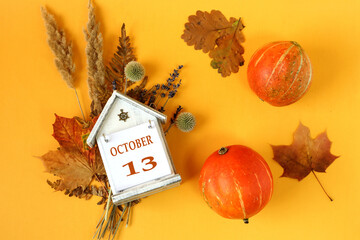 Calendar for October 13 : decorative house with the name of the month in English and the number 13 on bouquets of dried flowers, two orange pumpkins on a yellow background, top view