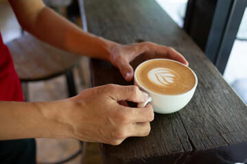Hand put a Latte arts coffe hot coffee on wooden table.barista love art concept.