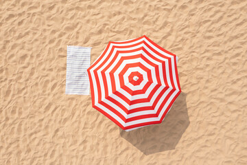 Striped beach umbrella near towel on sand, aerial view - Powered by Adobe