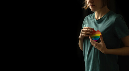 LGBT community background. Teenager girl holding colorful rainbow heart in hands on a black background with copy space