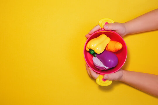 Child holds a pot with toy vegetables for soup in his hands on yellow background