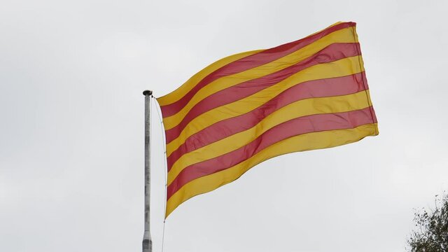 The official flag of Catalonia, Spain, is waving due to a strong wind on cloudy day. The colors of the striped flag are yellow and red.