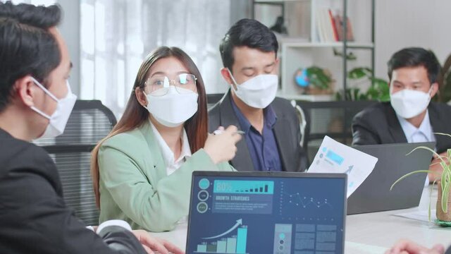 Young Asian Team Wearing Face Mask Have Meeting In A Conference Room. They Share Opinions, Statistics Show On Laptop Computer And Tv
