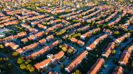 Aerial view of residential houses neighborhood and apartment building complex at sunset. Drone view of typical multi-level apartment building. Residential recreation concept. Warm light. 