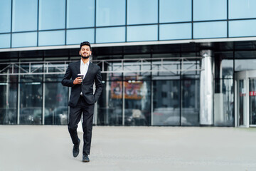 Fototapeta na wymiar A smiling bearded Indian man walks to an important meeting, behind him a modern building, he smiles and looks at the camera