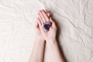 druse raw purple amethyst crystal on piece of stone on woman hand on grey linen