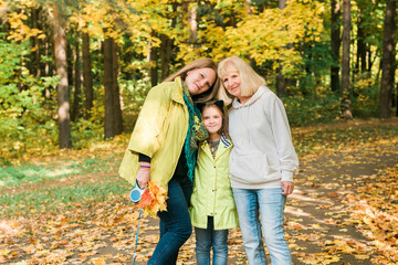 Portrait of three generations of happy beautiful woman looking at camera, hugging and smiling in autumn nature.