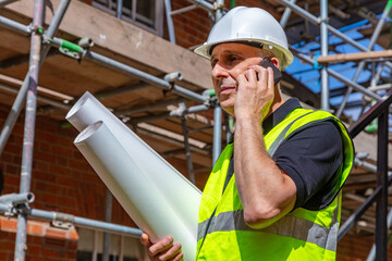 Male Builder Construction Worker on Building Site Using Phone and Plans