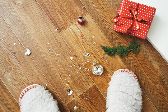 Top view of a Christmas tree, slippers and broken Christmas balls. The concept of unsuccessful preparation for the new year. A smashed red glass ball lies on the wooden floor.