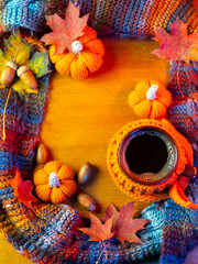 autumn colorful composition with coffee. A hot drink in a cup with a knitted jacket, a warm scarf, maple leaves and pumpkins. Autumn greeting card copy space