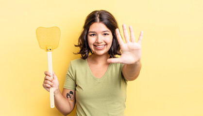 young hispanic woman smiling and looking friendly, showing number five. kill flies concept