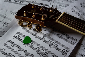 A guitar and a guitar pick are lying on sheets of sheet music.