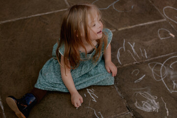 Little girl with Down Syndrome drawing and playing with chalk outdoors