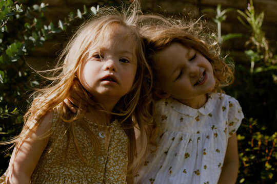 Twin girls with Down Syndrome sitting next to each other looking serious and happy