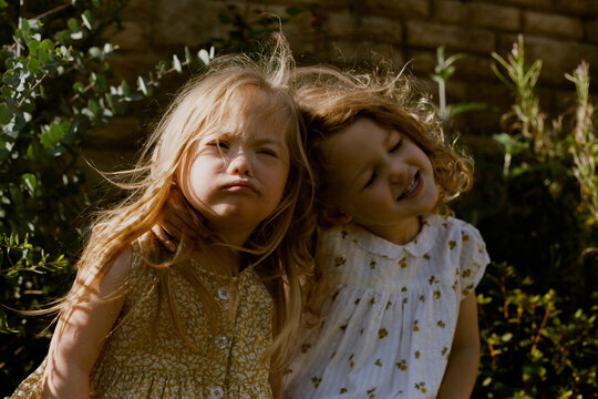 Twin girls with Down Syndrome sitting next to each other pouting and smiling