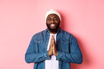 Happy smiling Black man saying thank you, holding hands in pray or namaste gesture, standing...