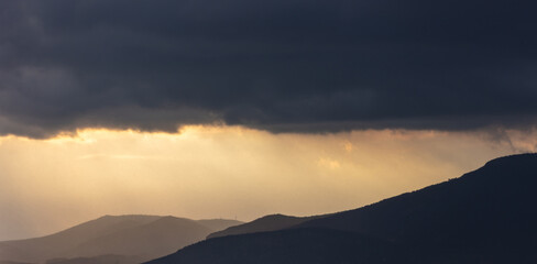 Heavy dark clouds on sky over mountains at sunset. Cumulus dark gray color cloudscape