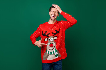 Photo portrait smiling man pointing at funny knitted sweater with reindeer laughing isolated green...