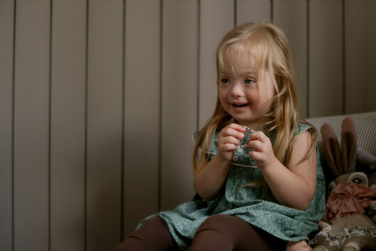 Portrait of little girl with Down Syndrome sitting on chair and laughing