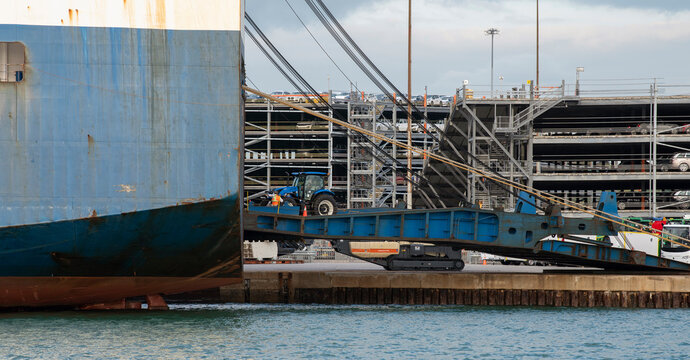 Southampton docks, England, UK. 2021. Farm tractor being loaded onto roro commercial ship via a ramp on the dockside.