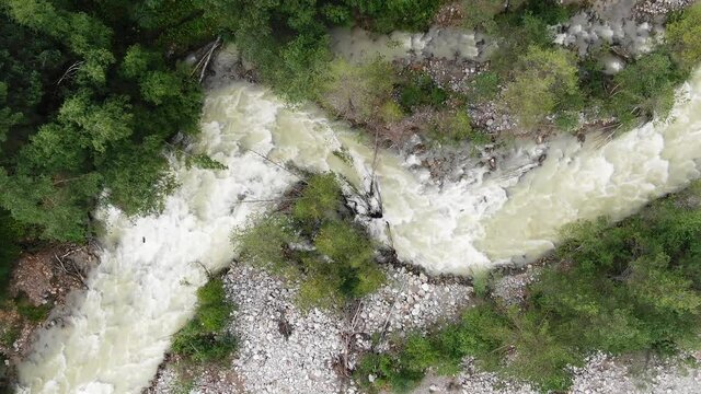 Rough mountainous foamy river with fast water streams runs winding between rocky and steep forestry banks aerial zoom in