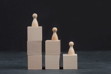 Three wooden persons are standing on cubs in different heights, dark background