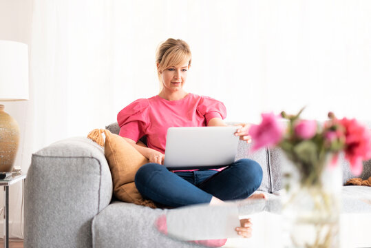 Blond haired middle aged woman working laptop while sitting on a couch