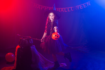 Little girl with funny tricky face pretend like flying on the broom on Halloween holiday. Kid girl wear witch costume. Fantasy, fairy tale and masquerade concept.