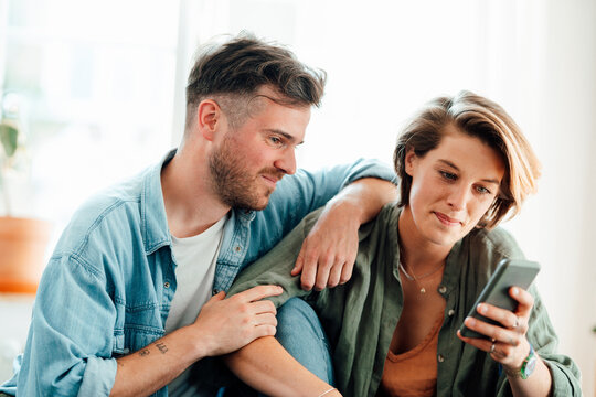 Man sitting near woman using smart phone at home