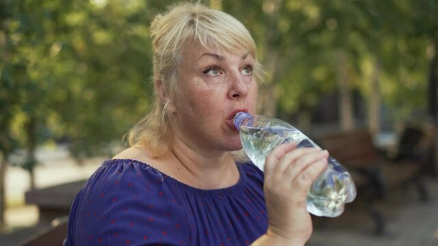 Fat woman drinking water at the street