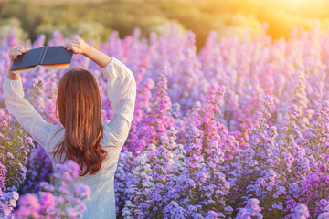 girl in vintage dress sits holding Bible to read and study God's teachings alone on blurred...