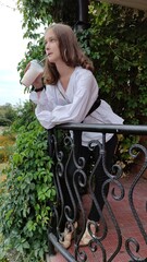 A beautiful girl in a white blouse is drinking coffee in the park
