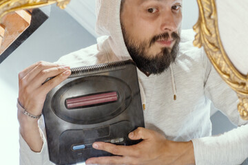 A man who grew up in the 90s is nostalgic for the times of 16-bit gameplay and holds a retro video game console in his hands