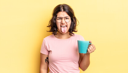 young hispanic woman feeling disgusted and irritated and tongue out. coffee mug concept