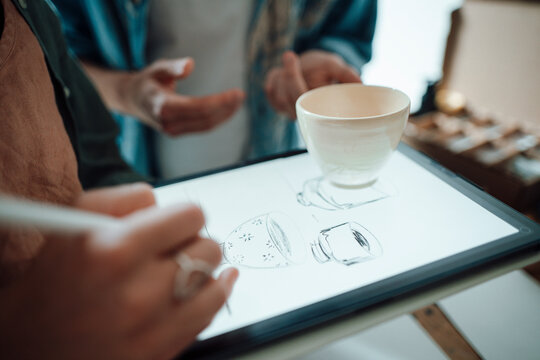 Female artist making cup sketch on graphic tablet while working at home office
