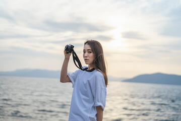 夕暮れの海で写真を撮るカメラ女子