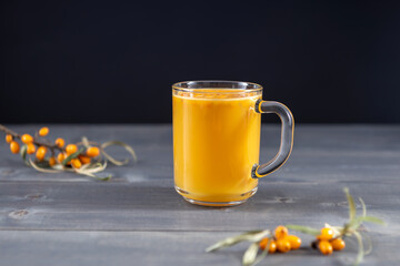 a glass mug of sea buckthorn juice and fresh sea buckthorn berries on a wooden table