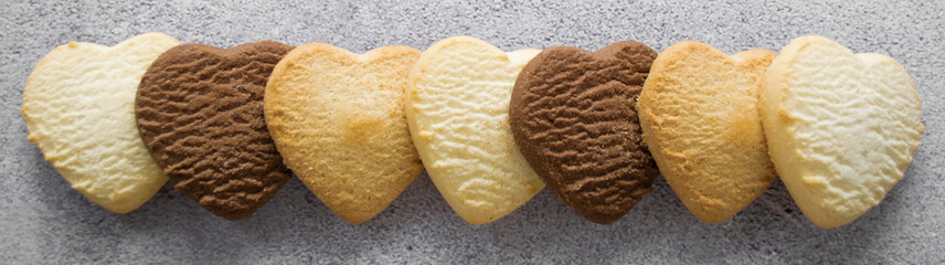 Banner with multicolored cookies in the shape of a heart: vanilla, lemon, chocolate. Gray background, copy space