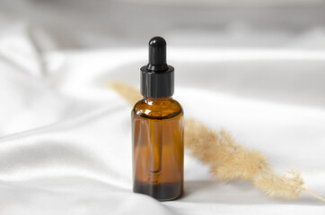 Essential oil or serum in a brown bottle with a dropper. A bottle of aromatic oil on a white silk...