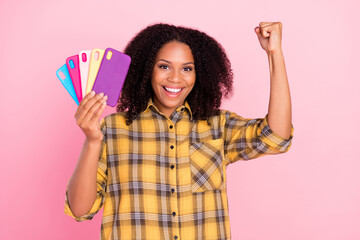 Photo of astonished lady hold fan phone case celebrate victory raise fist wear plaid shirt isolated pink color background