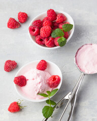 Fresh raspberries with mint and homemade ice cream in a white cup on a light background. Stainless steel spoon for ice cream balls. Delicious and romantic dessert. Top view. Copy space