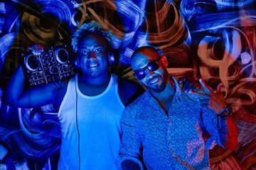 African-American DJ in a white T-shirt with a DJ console and headphones is photographed with a Latin American male friend in a club against a wall with graffiti
