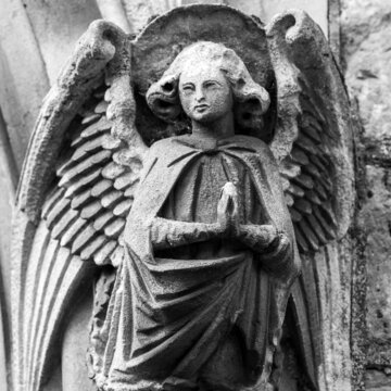 Angel looking sculpture, part of stone arch, hands in prayer